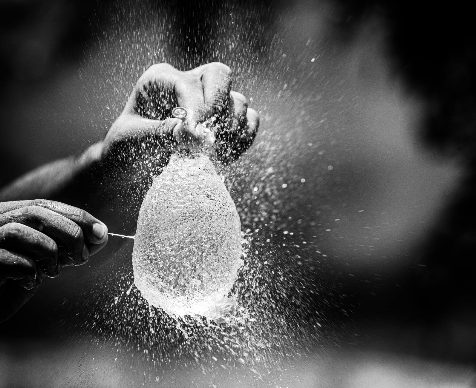 grayscale photo of person popping a water balloon