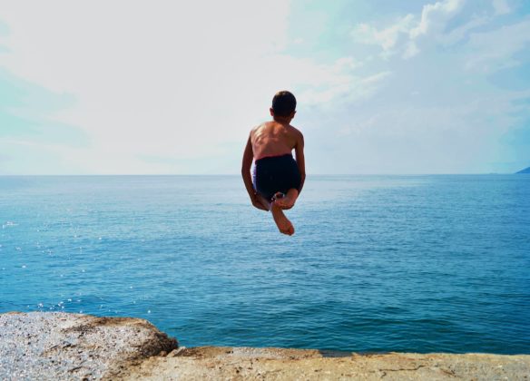 time lapse photography of boy in black shorts jumping on body of water