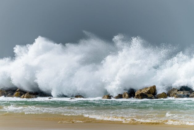 waves splashing in stormy ocean near boulders and sandy beach