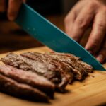 person slicing meat on brown chopping board