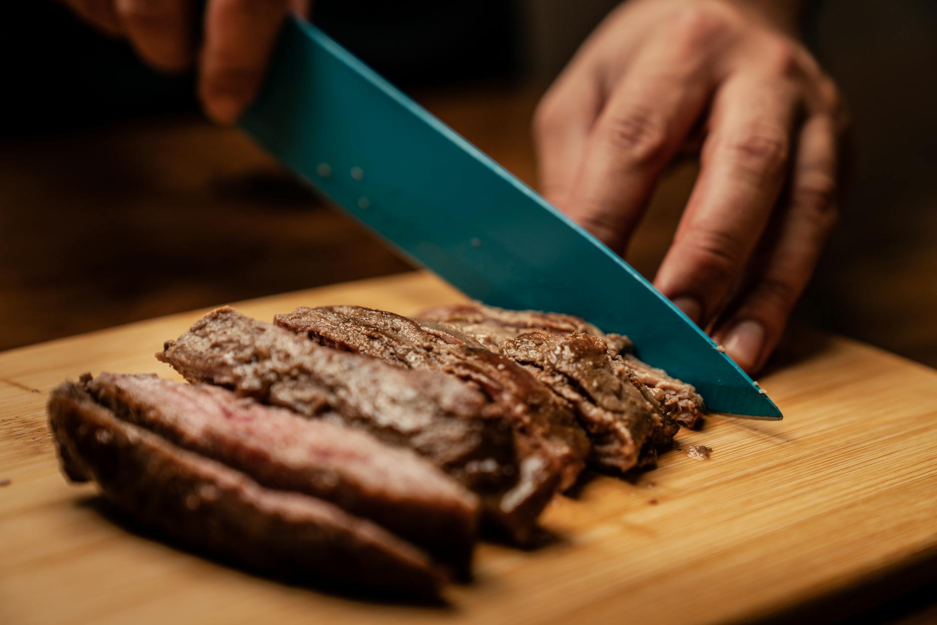 person slicing meat on brown chopping board